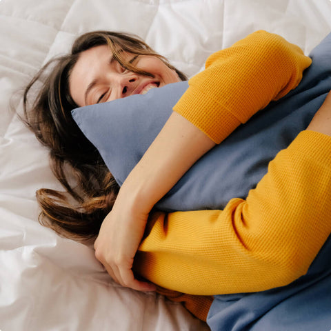 A woman smiling and holding a Slumber Cloud pillow with an Essential Pillowcase