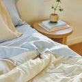 The morning sun shining onto a side table and bed made with Slumber Cloud products