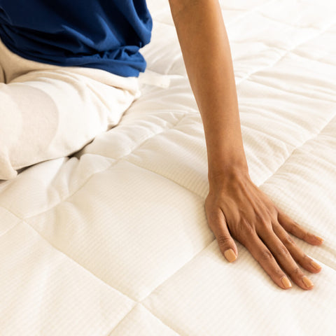A woman touching the outer fabric of the Slumber Cloud Performance Mattress Pad.