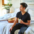 Man drinking coffee on his bed with the Slumber Cloud Performance Duvet Cover with temperature regulation technology and Tencel in the morning.